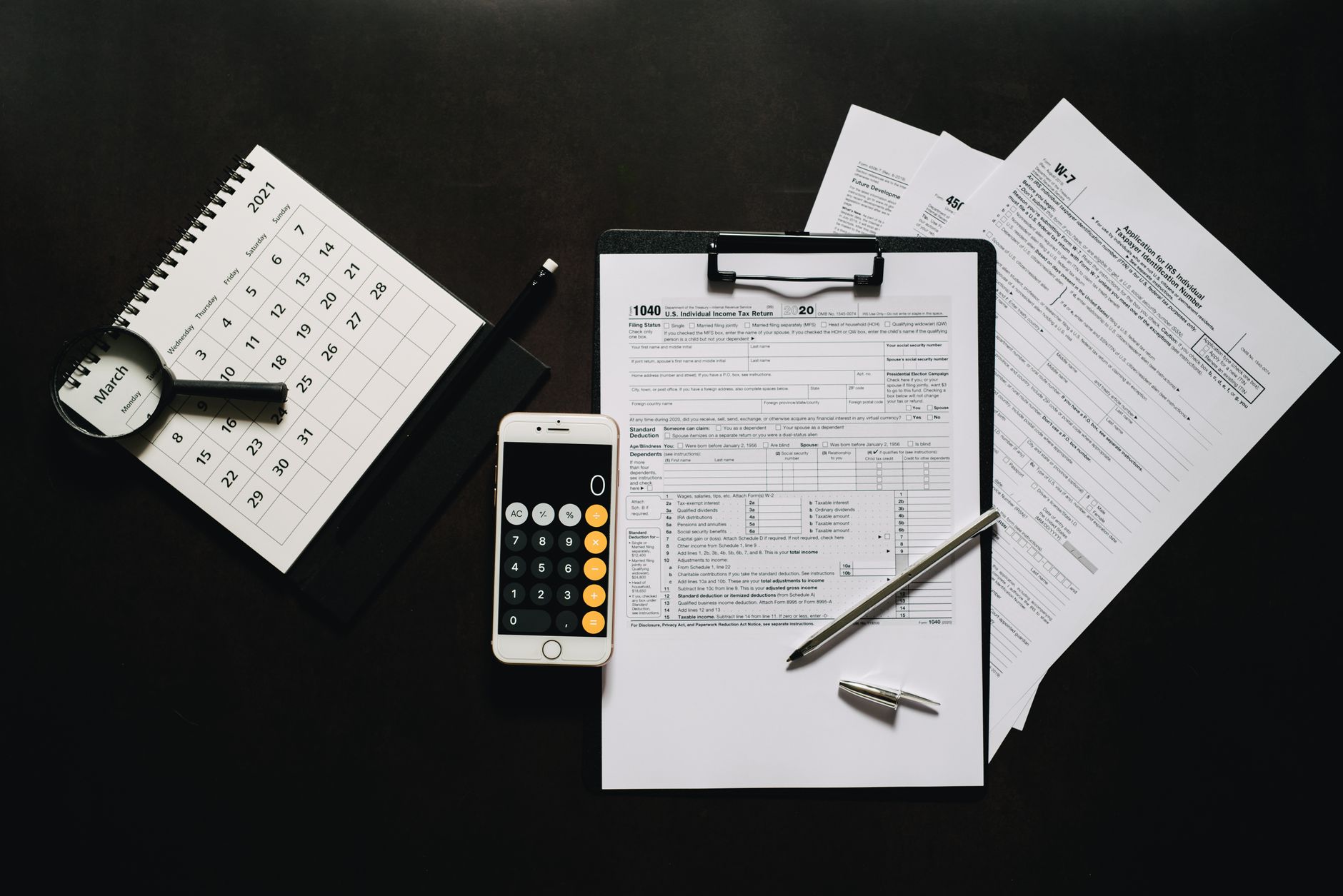 Tax registration forms, calculator, calendar, and magnifying glass on a dark desk surface representing BIR Form 2303 compliance requirements