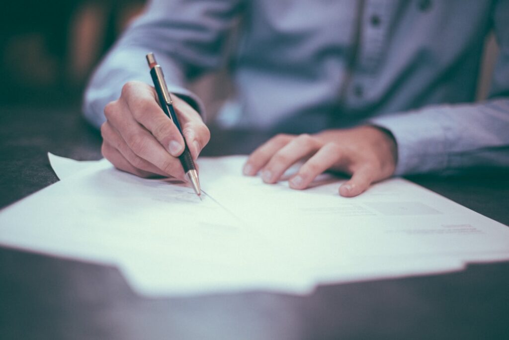 Close-up of a person signing a legal document or contract with a pen — red flags to watch for when hiring a law firm