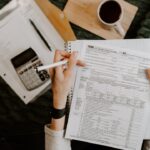 Person reviewing a tax registration form with a calculator, coffee cup, and laptop on the desk — illustrating BIR Form 1901 filing for freelancers in the Philippines
