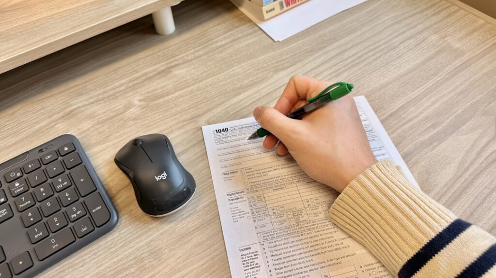 Hand filling out a tax form on a desk with a keyboard and mouse nearby, representing the step-by-step BIR Form 1901 online filing process via ORUS